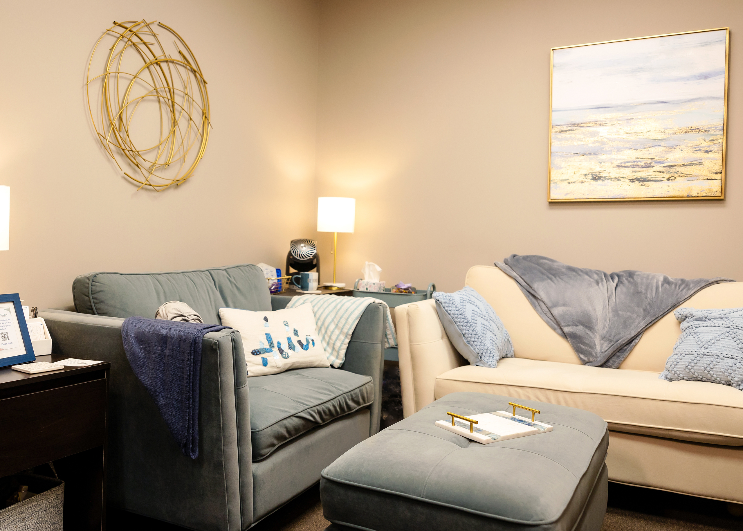 Soft couches with pillows and throw blankets are warm, offering comfort in a well, but softly lit space. Neutral beige walls and simple art tastfully decorates the walls. 