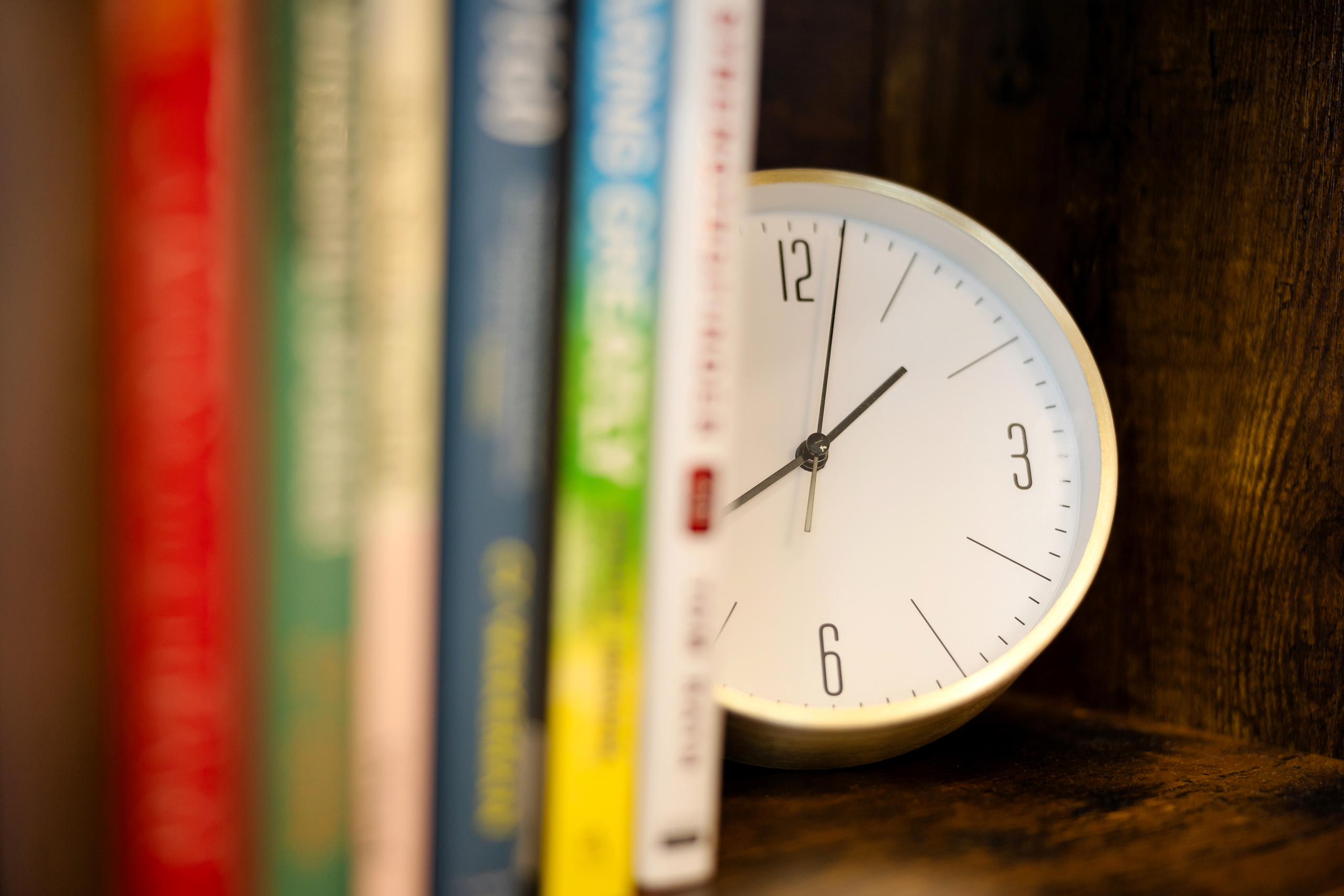 Colorful books are seen in the foreground with a clock sitting on the shelf beside them. When searching for a "therapist near me" be sure to consider if the space you'll be meeting in suites your needs. 