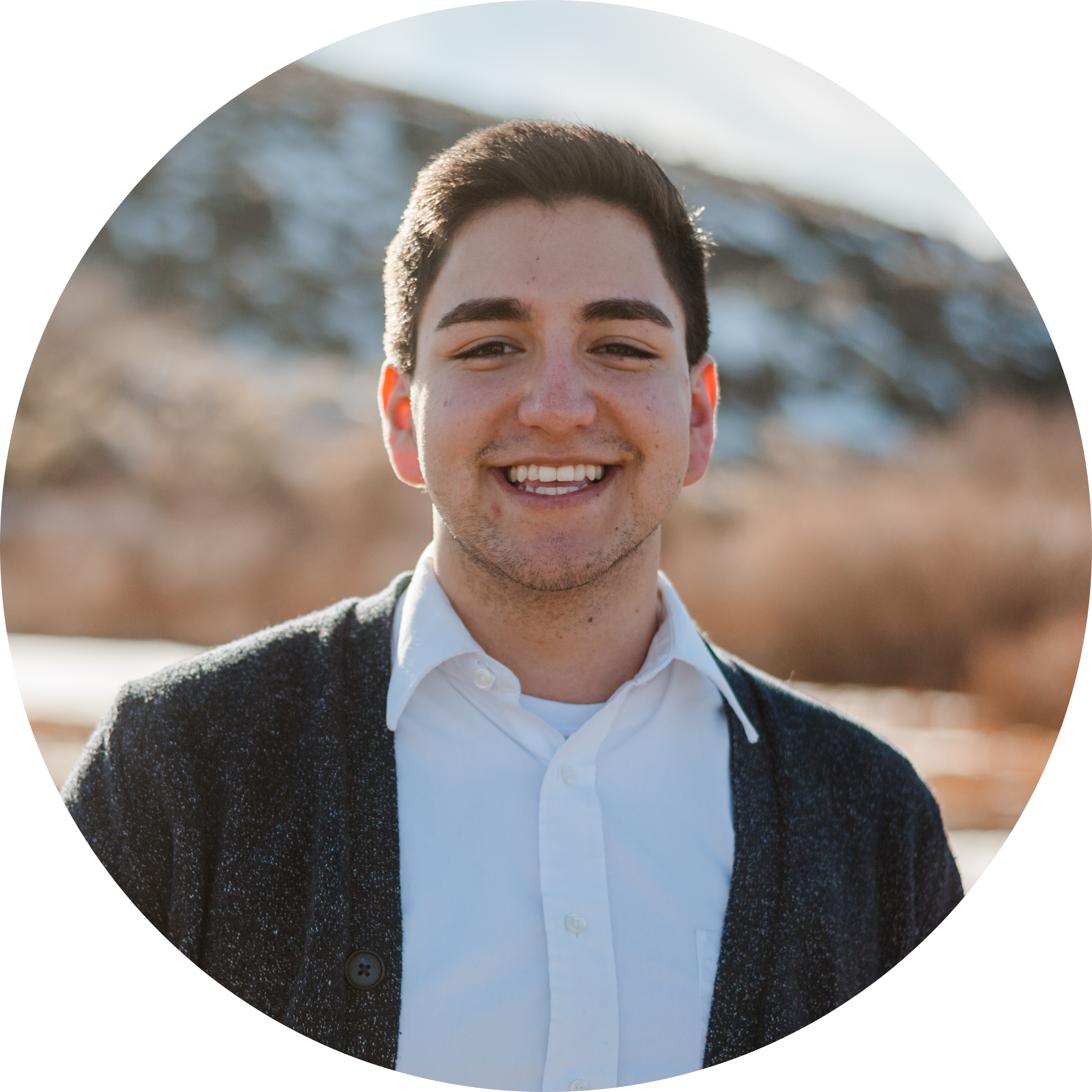 Image of young Hispanic man smiling and standing in front of a snowy hill on a sunny day.